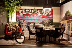 a dining room table with chairs and a bike parked next to it in front of a graffiti covered wall