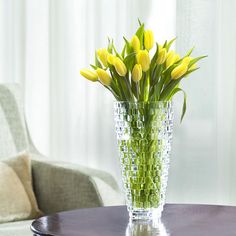 a vase filled with yellow flowers sitting on top of a table next to a chair