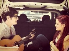 two people sitting in the back of a car playing guitar and singing to each other