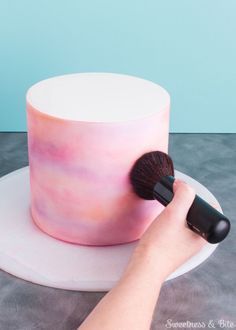 a person holding a brush to a pink cake