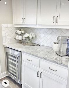 a white kitchen with marble counter tops and stainless steel appliance in the corner