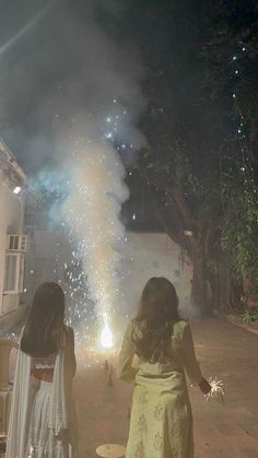 two women standing next to each other with fireworks in the sky behind them and onlookers watching