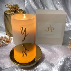 a lit candle next to a gift box on a white tablecloth with gold decorations