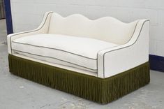 a white and green couch sitting on top of a cement floor next to a wall