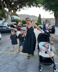 a woman in a black dress is walking with two small boys and a baby stroller