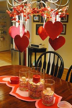 a dining room table with hearts hanging from the chandelier and plates on the placemats