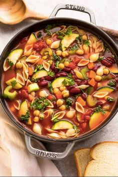 a pot filled with pasta and vegetables next to bread