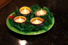 four lit candles sitting on top of a green plate covered in tissue paper and leaves