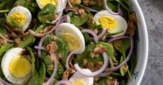 a salad with hard boiled eggs, onions and spinach in a blue and white bowl