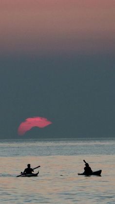 two people in canoes paddling on the water at sunset with pink and blue sky