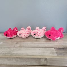 three crocheted pink and white fish sitting on top of a wooden table next to each other