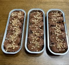 three tins filled with brownies and nuts on top of a wooden table next to each other