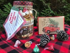 a mason jar filled with candy and pine cones next to a christmas card on a plaid table cloth