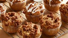 a bunch of muffins sitting on a cooling rack with icing drizzled around them