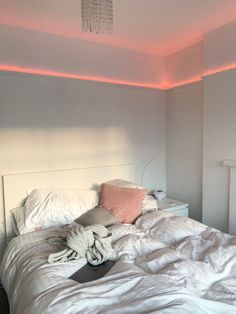 an unmade bed with white sheets and pillows in a room that has pink lights on the ceiling