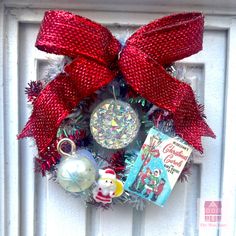 a red christmas wreath with ornaments hanging on the front door and an ornament attached to it