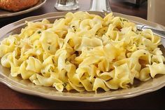 a white plate topped with pasta on top of a wooden table next to silverware