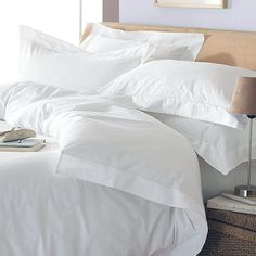 an unmade bed with white sheets and pillows on top of it next to a lamp