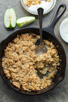 an apple crisp in a cast iron skillet with two plates and spoons next to it