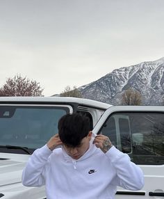 a man standing in front of a white truck with mountains in the backgroud