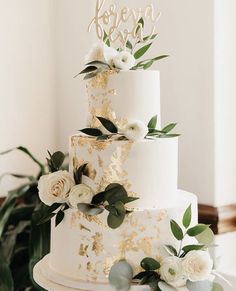 a white and gold wedding cake with greenery