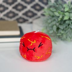 a red pillow sitting on top of a white table next to a green potted plant