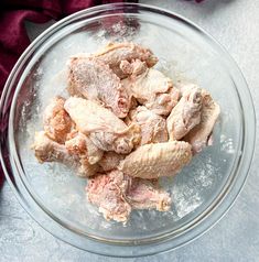 a glass bowl filled with raw chicken on top of a table