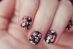 a woman's hand with black and pink flowers on it, holding onto her nails