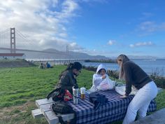 two women are sitting at a picnic table near the golden gate bridge while another woman is standing next to her