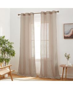 a living room with white walls and wooden floors, two windows covered in sheer curtains