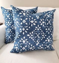 two blue pillows sitting on top of a white couch