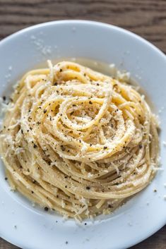 a white plate topped with pasta covered in parmesan and seasoning on top of a wooden table