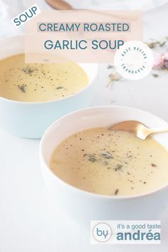 two bowls of creamy roasted garlic soup on a white table with spoons and flowers in the background