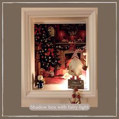 a shadow box with fairy lights in front of a christmas tree and other items on the shelf