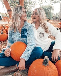 two women sitting on the ground with pumpkins in front of them and one is smiling