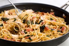 a fork is being used to stir pasta in a skillet with chicken and spinach