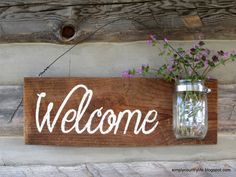 a wooden sign that says welcome with flowers in a mason jar hanging on the wall