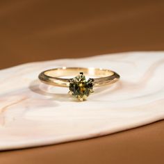 a gold ring with a green diamond on top of a white marble slabd surface