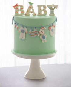 a baby shower cake on a white pedestal with green frosting and decorations hanging from the top