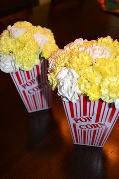 two red and white striped popcorn boxes with flowers in them on a wooden table top