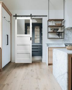 a kitchen with white walls and wooden floors, an open door leading to the dining room