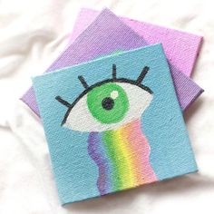 two small coasters with an eye on one and a rainbow on the other, sitting on a bed