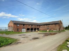 an old brick building sitting on the side of a dirt road next to a field