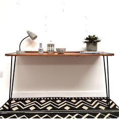 a wooden table with two plants on top and a rug underneath it in front of a white wall