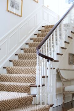 a staircase with beige carpet and white banisters on the bottom, next to a chair