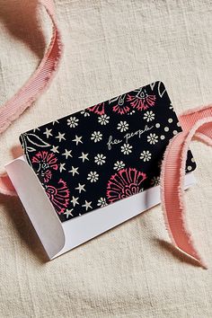 a black and white card with pink ribbon next to it on a cloth covered surface