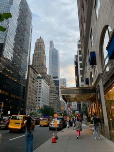 people are walking down the sidewalk in front of tall buildings and skyscrapers on a cloudy day