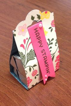 an origami box with a pink ribbon on it sitting on a wooden table