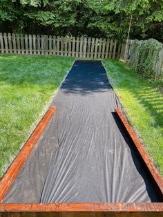 a long wooden walkway in the middle of a yard with grass and trees behind it