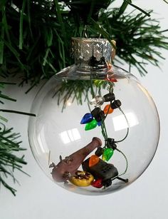 an ornament hanging from a christmas tree filled with toys and lights, on top of a pine branch